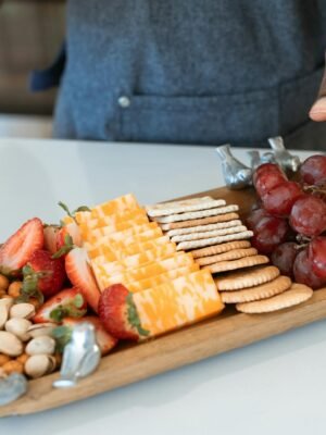 An elegant cheese and fruit platter with crackers, nuts, and berries on a wooden serving board.