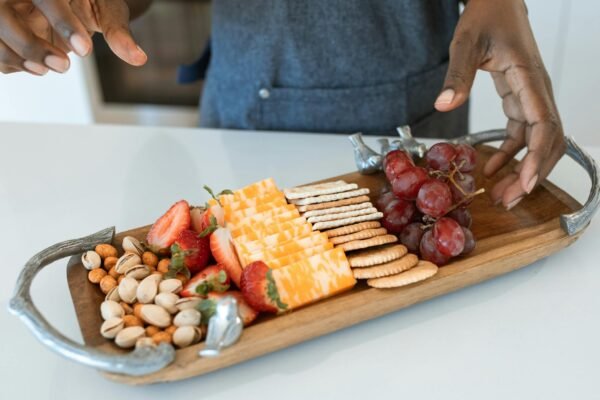 An elegant cheese and fruit platter with crackers, nuts, and berries on a wooden serving board.