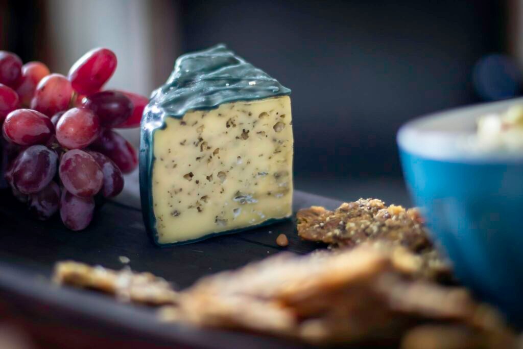 Close-up of gourmet cheese served with grapes and crackers on a dark platter.