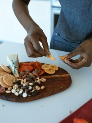 Close-up of hands arranging a delicious charcuterie board with cheese, nuts, and dried fruits.