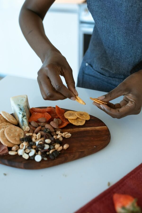 Close-up of hands arranging a delicious charcuterie board with cheese, nuts, and dried fruits.